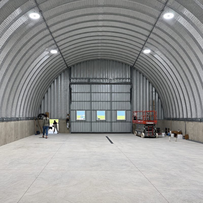 Inside a Q Series Quonset hut: an open concrete floor under the rounded arch, with a large overhead door at the far end