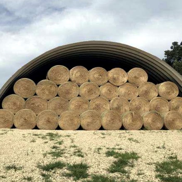 Round hay bales stacked under an open-ended Quonset hut