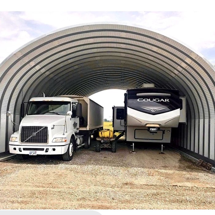 A semi truck, a fifth-wheel RV and a utility vehicle parked inside an open Quonset hut
